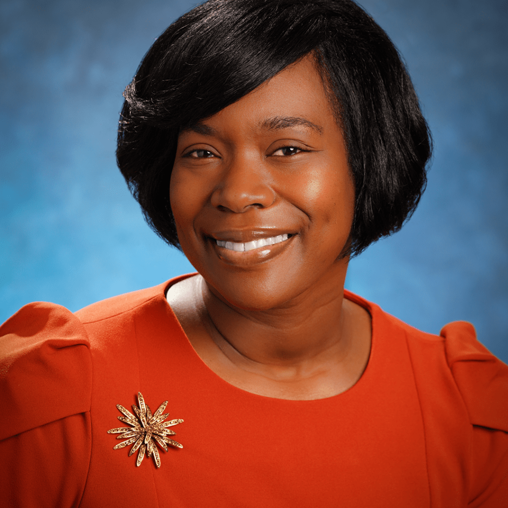 Robin Walton smiling in a red dress with a gold pin