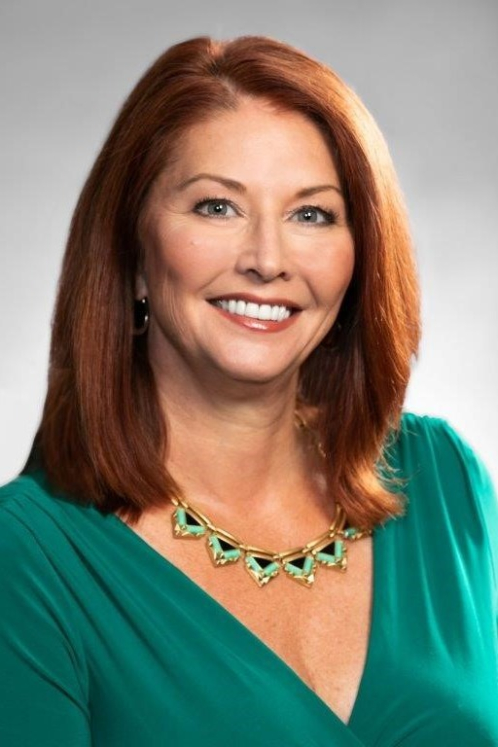 Lisa Morina is a woman with light skin and reddish hair who is smiling and wearing a green dress with a v neckline.