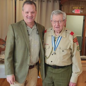 Brad Denn stands on the left wearing a loden-green sport coat and Lee Bealuk stands on the right wearing a Scouts BSA field uniform and Silver Beaver Award blue-and-white ribbon.