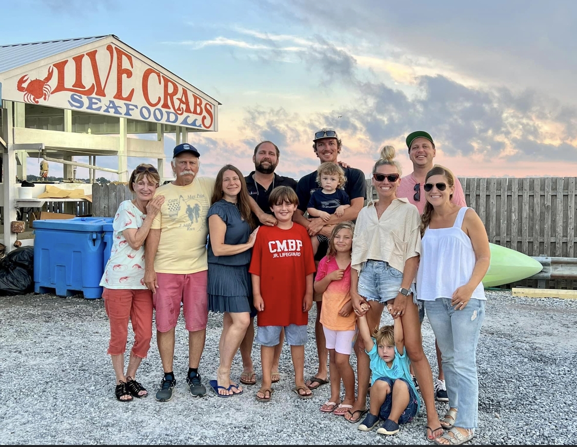 A large multi-generational family stands together on a beach